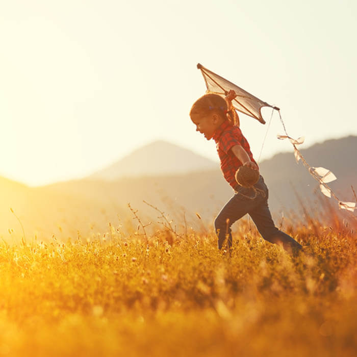 Little boy running, launching a kite at sunset